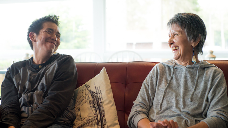 a man and a woman sit on a couch smiling at one another