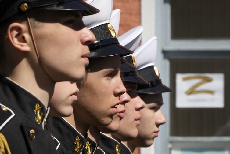 Young Navy school cadets march. Sheets of paper with the letter Z, a symbol of the Russian military, displayed in windows in the background.
