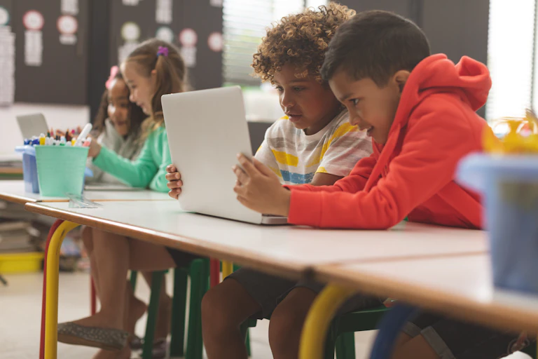 Students sitting at a desk looking at a laptop.