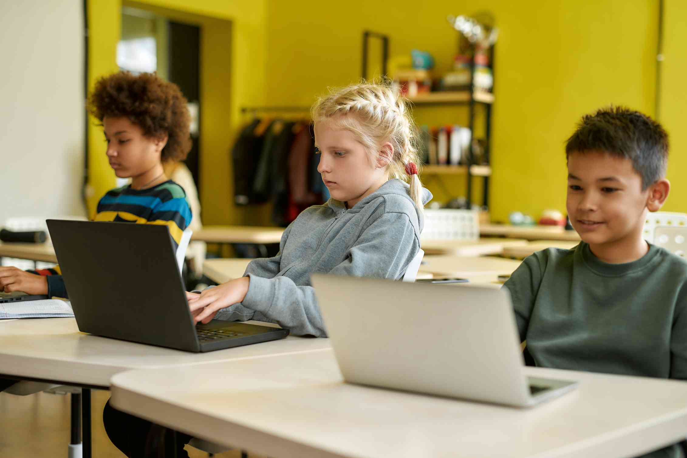 Children are seen at desks working on laptops.
