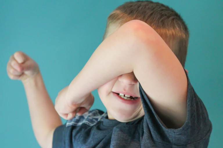A young boy uses his arm to shield his face.