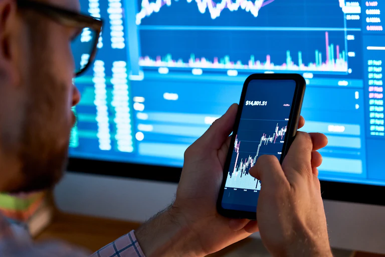 Photo of a man looking at a phone showing a stock price chart.