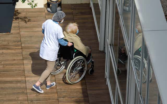 Nurse pushes elderly resident inside an aged care facility.