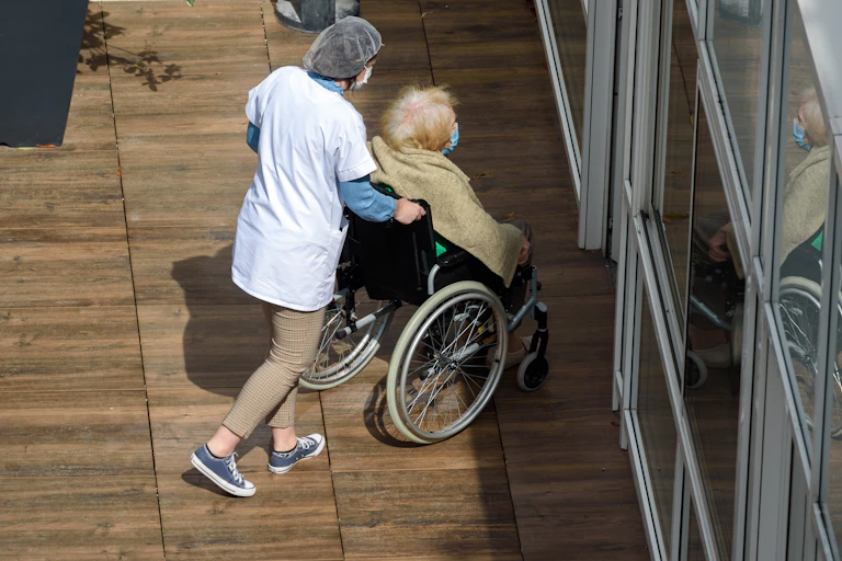 Nurse pushes elderly resident inside an aged care facility.