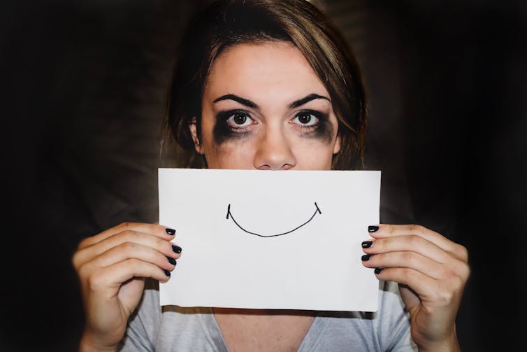 Woman with tear-streaked face, holding up a smiling mouth on a piece of paper