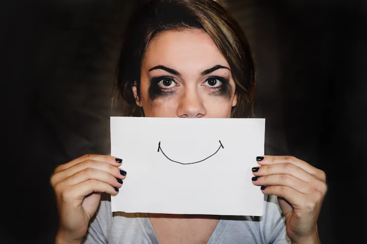 Woman with tear-streaked face, holding up a smiling mouth on a piece of paper