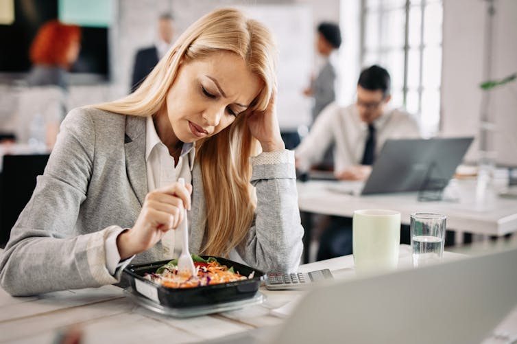 Women with ADHD eating lunch at her desk. She looks unhappy. 