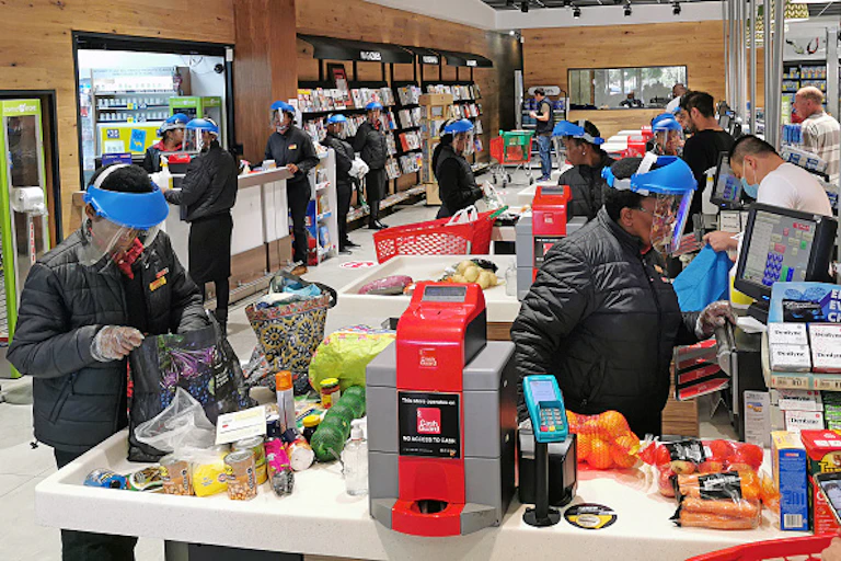 People in a supermarket with vegetables and protective gear.