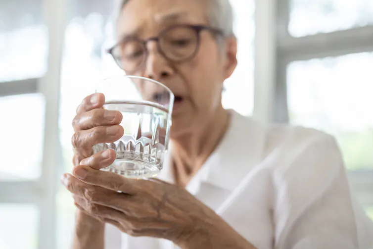 Woman holding her wrist to steady it so she can drink a glass of water.