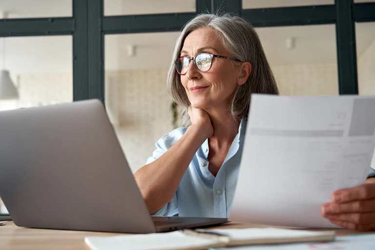 Une femme regarde l'écran de son ordinateur, une feuille de papier à la main