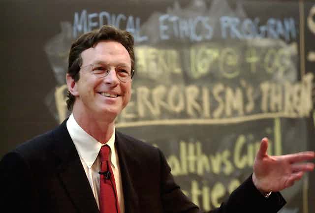 Michael Crichton sonriendo con la mano levantada
