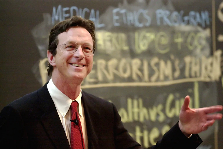 Michael Crichton sonriendo con la mano levantada
