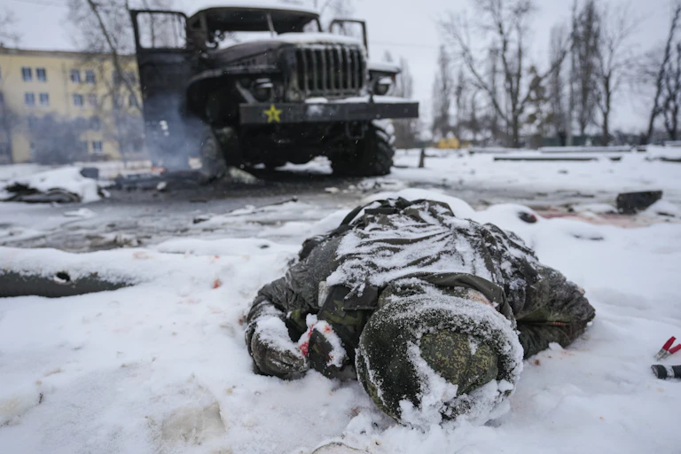 A body lies in the snow next to a truck