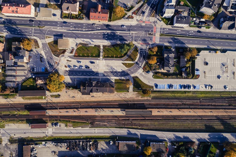 An aerial view of a city centre with railway tracks, paved parking lot, roads and several small scattered green spaces.