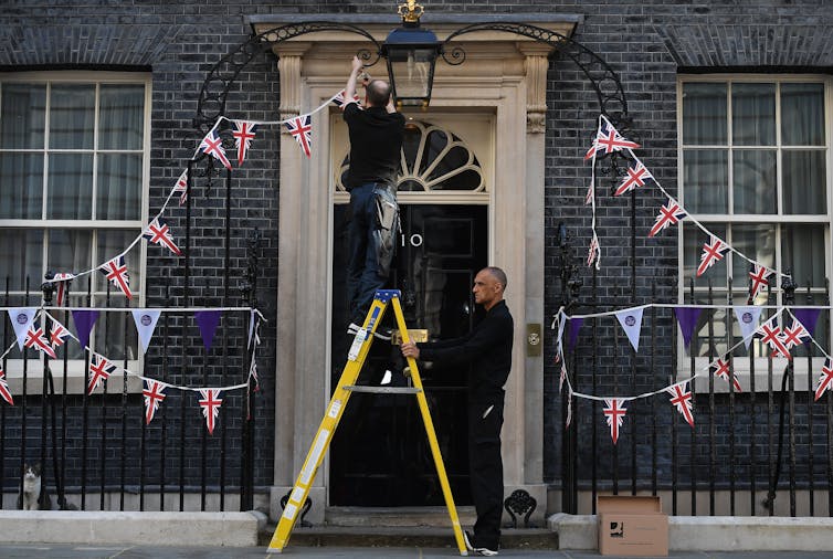 Workers on a stepladder remove Jubilee bunting form around the entrance to 10 Downing Street, June 2022.