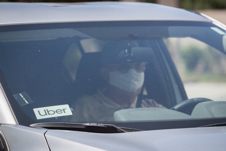 man wearing a mask driving a car with an Uber badge