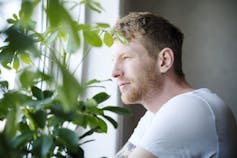 A man in a T-shirt stares out a window.