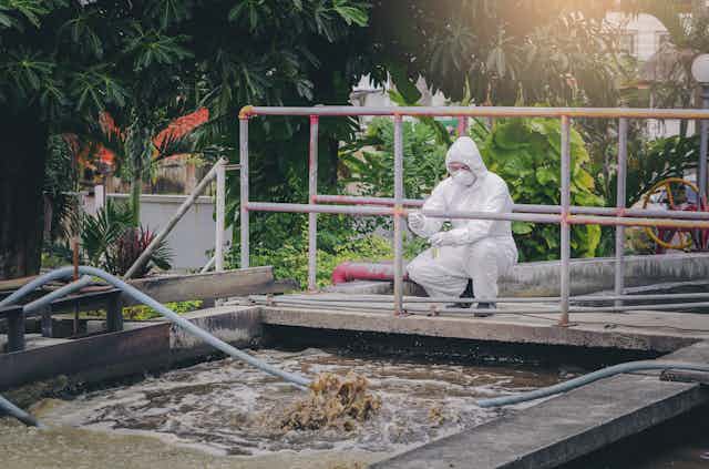 a person in a white hazmat suit crouches near a vat of wastewater