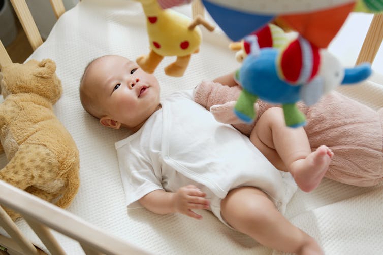 baby lying on back in crib looking up at mobile suspended from above