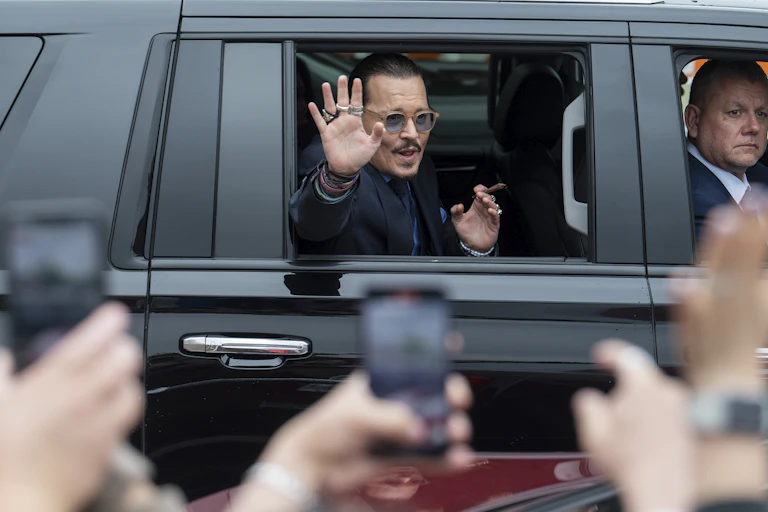 A man sits in the backseat of an SUV with a cigar in one hand as he waves to people with the other