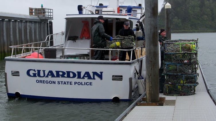 Men on a police boat unload crab traps onto a dock.