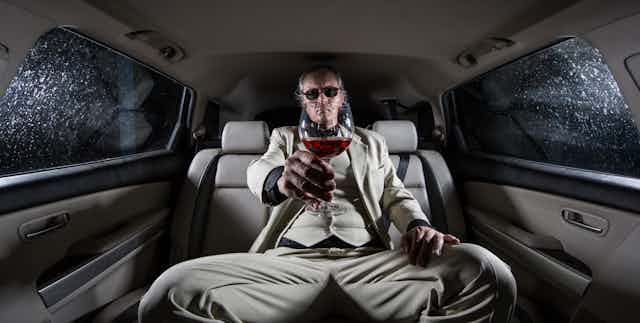 Well-dresssed man with glass of wine in back of a limo.