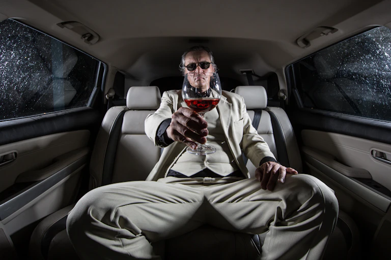 Well-dresssed man with glass of wine in back of a limo.