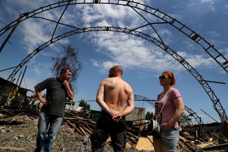 Three men standing in front of a damaged building.