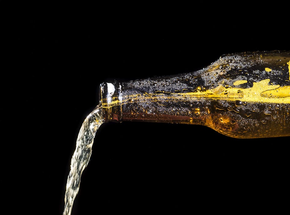 Alcohol flows out the spout of a clear brown bottle that is turned horizontal.