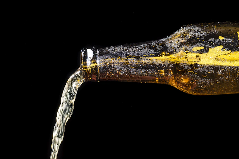 Alcohol flows out the spout of a clear brown bottle that is turned horizontal.
