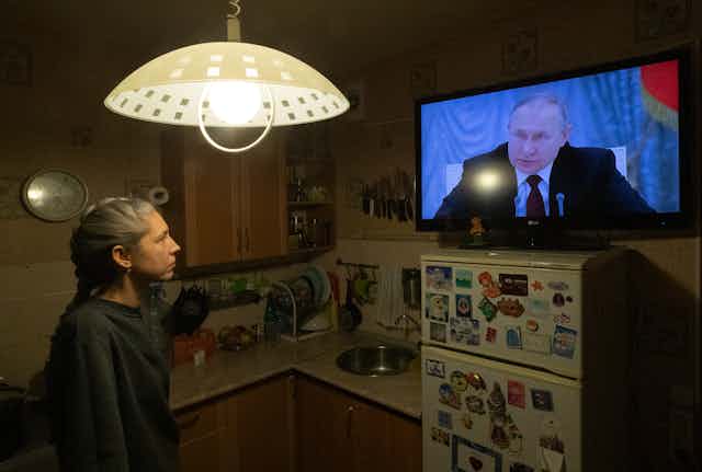 Woman in kitchen watching Putin on TV.