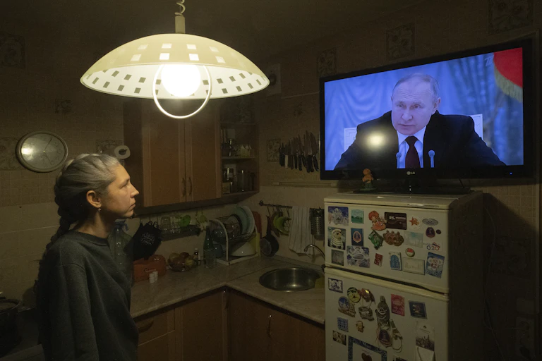 Woman in kitchen watching Putin on TV.