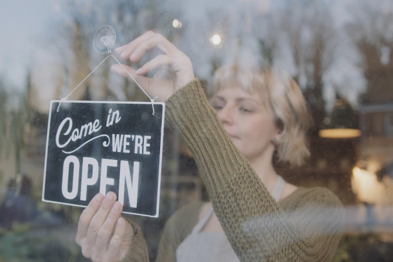 Woman hangs 'open' sign at shop front.