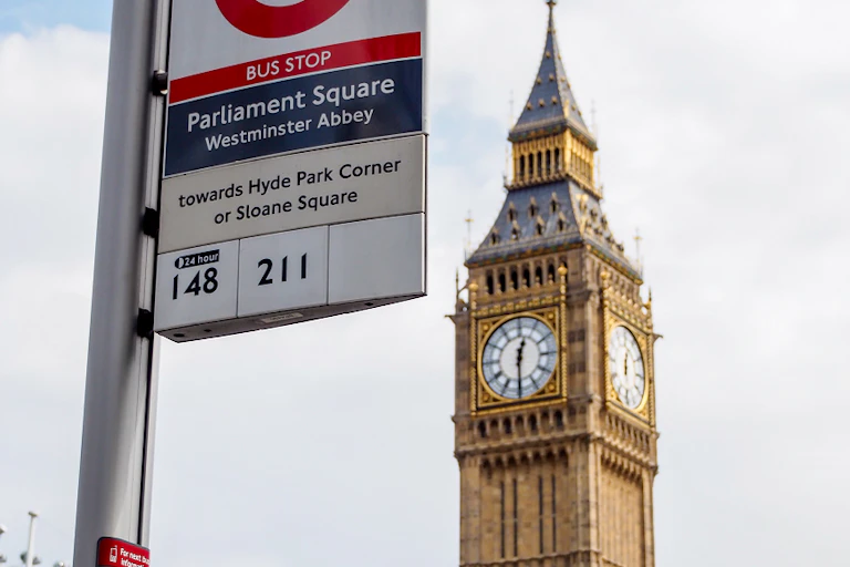 A bus srtop in Parliament SQuare in London showing that the number 148 and 211 buses stop there. In the background is Big Ben.