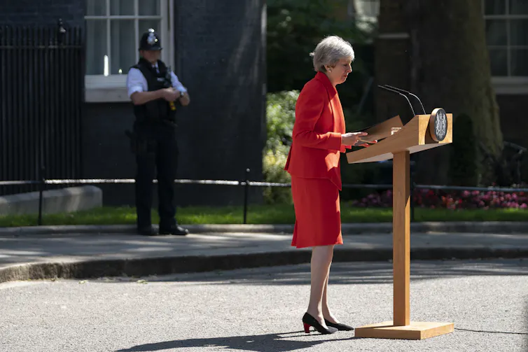 Wide shot of Theresa May in a red skirt suit speaking at a podium outside of number 10 Downing Street