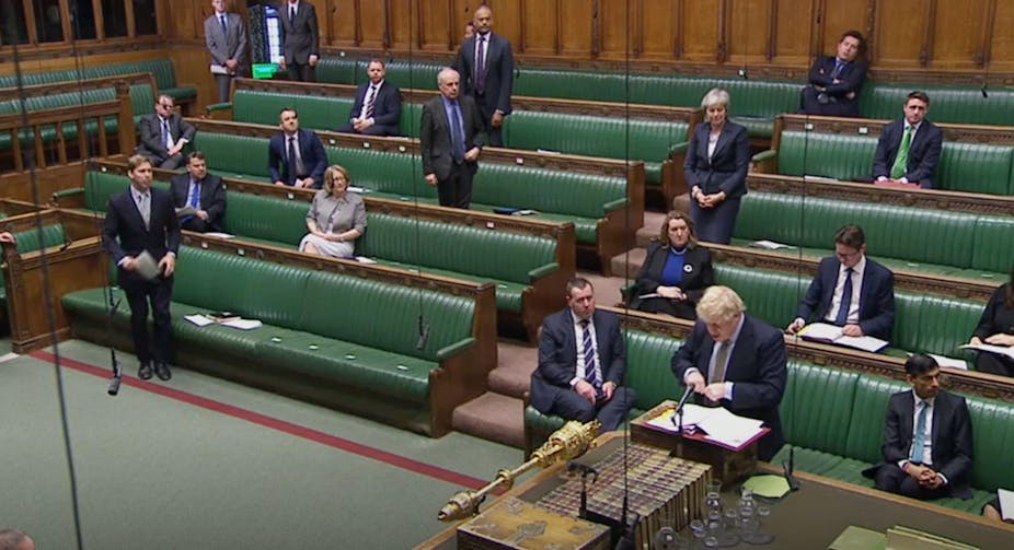 Wide view of Boris Johnson speaking in a mostly empty Commons Chamber with a smattering of MPs sitting in the green benches behind him