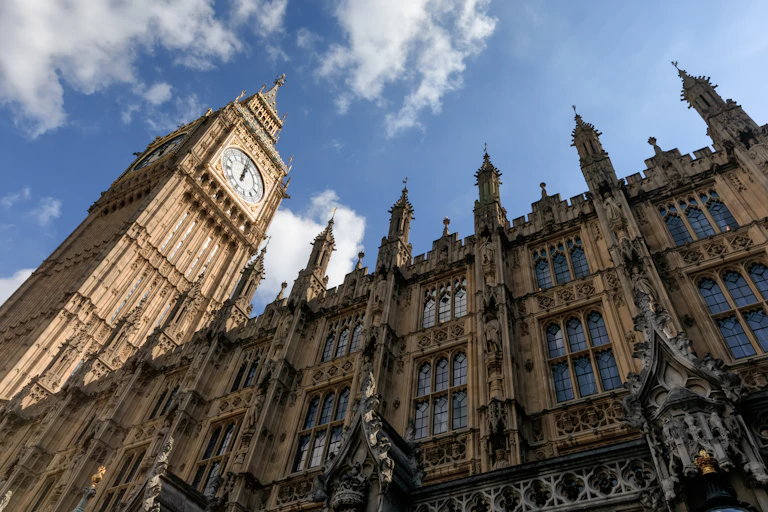 View from the ground of Big Ben and the houses of Parliament looming against a blue sky with clouds