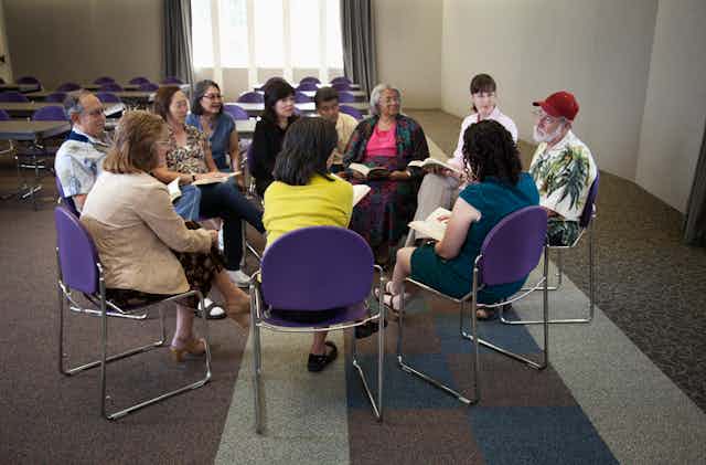 People sitting in a circle and having a discussion around  a book.