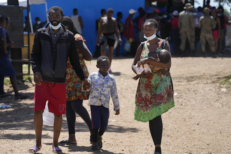A young woman holds a baby with a boy and a man next to her.
