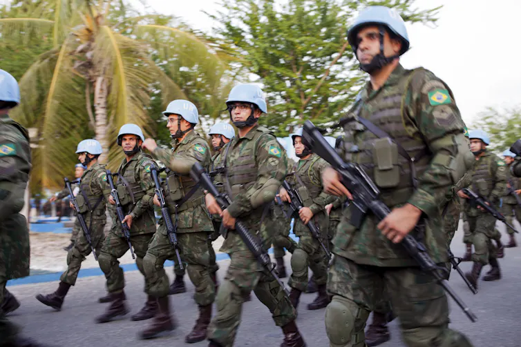 Armed soldiers carrying weapons walk in formation.