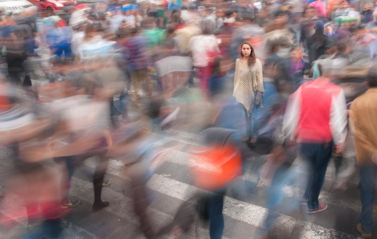 a woman stands among a crowd of people moving around her