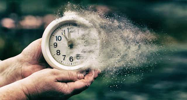 A pair of hands hold a disintegrating white round clock