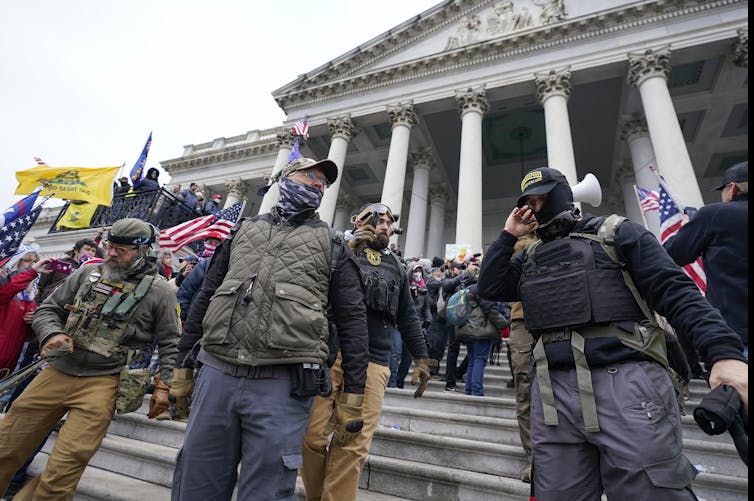 People in hats, masks and protective gear stand in front of a portico