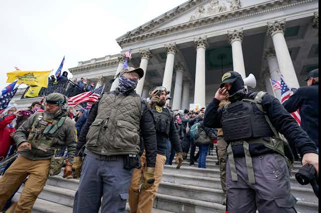 People in hats, masks and protective gear stand in front of a portico
