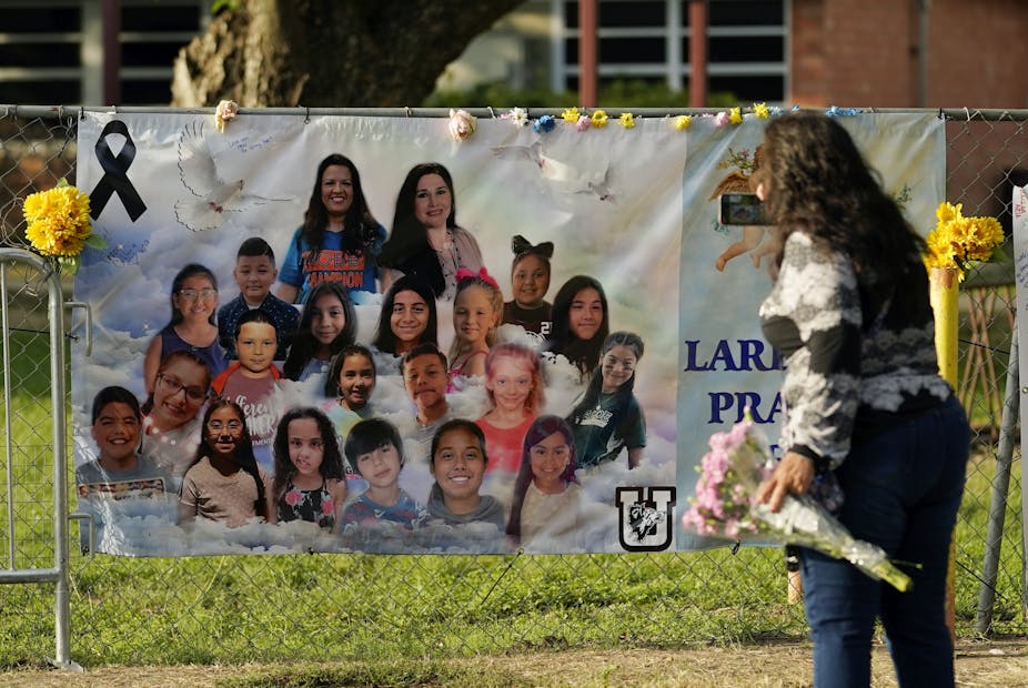 A woman holding flowers looks at a banner with photos of children.