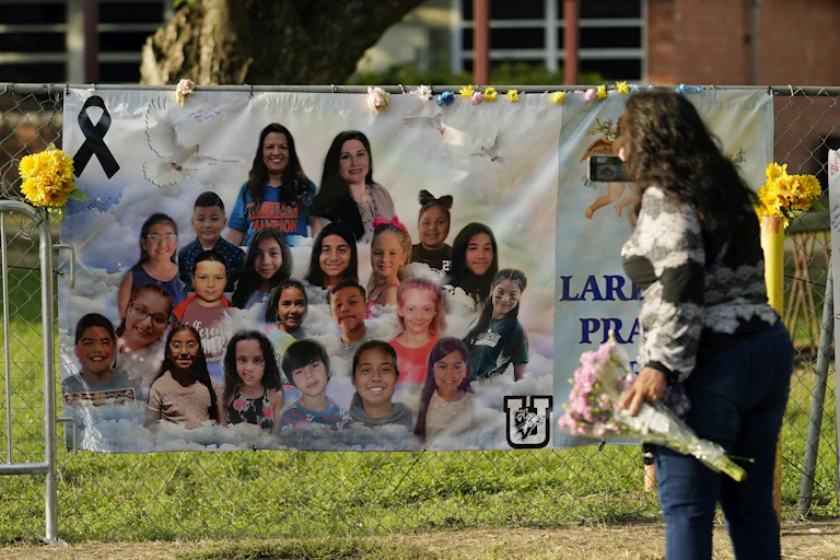 A woman holding flowers looks at a banner with photos of children.