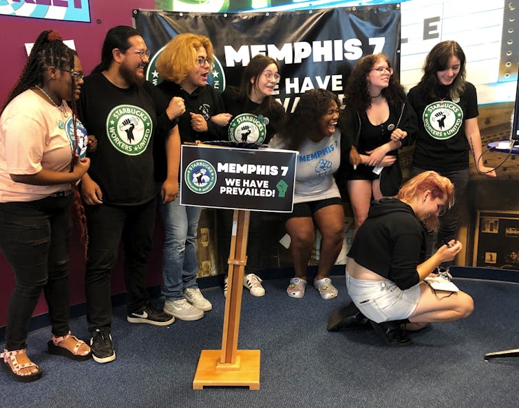 A group of diverse workers mostly standing and wearing black Memphis 7 t-shirts celebrate victory