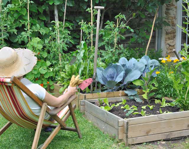 woman in hat sits and looks over garden