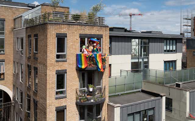 cityscape with one balcony of people celebrating gay pride with rainbow flags