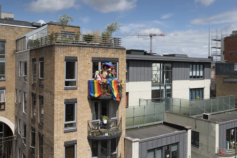 cityscape with one balcony of people celebrating gay pride with rainbow flags